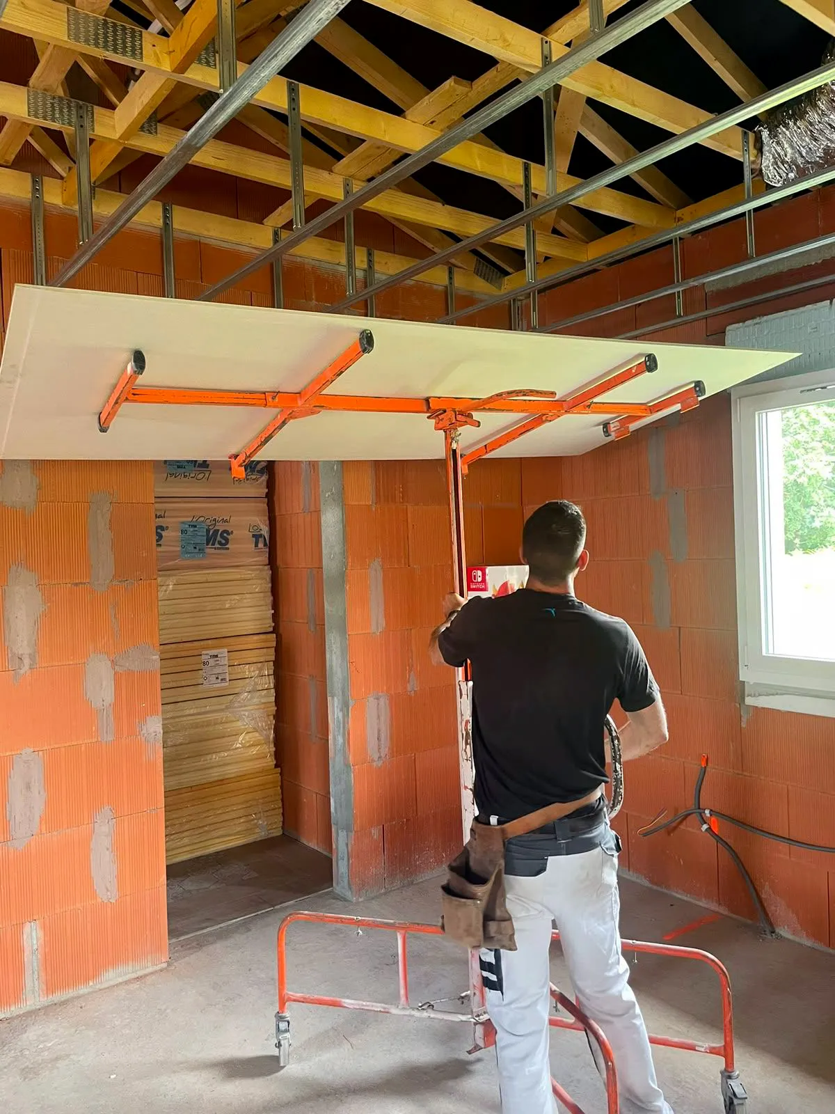 Sébastien Harre sur un chantier, posant une plaque de plâtre au plafond à l'aide d'un lève-plaque